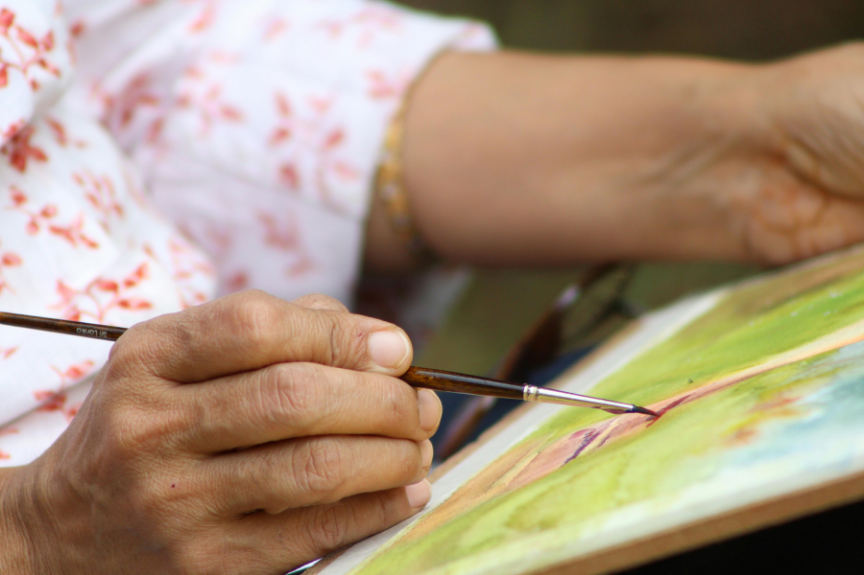 Hand mit Pinsel beim Arbeiten mit Farbe und unterschiedlichen Materialien